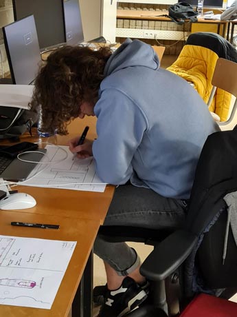 jeune adulte penché sur un bureau en train de dessiner